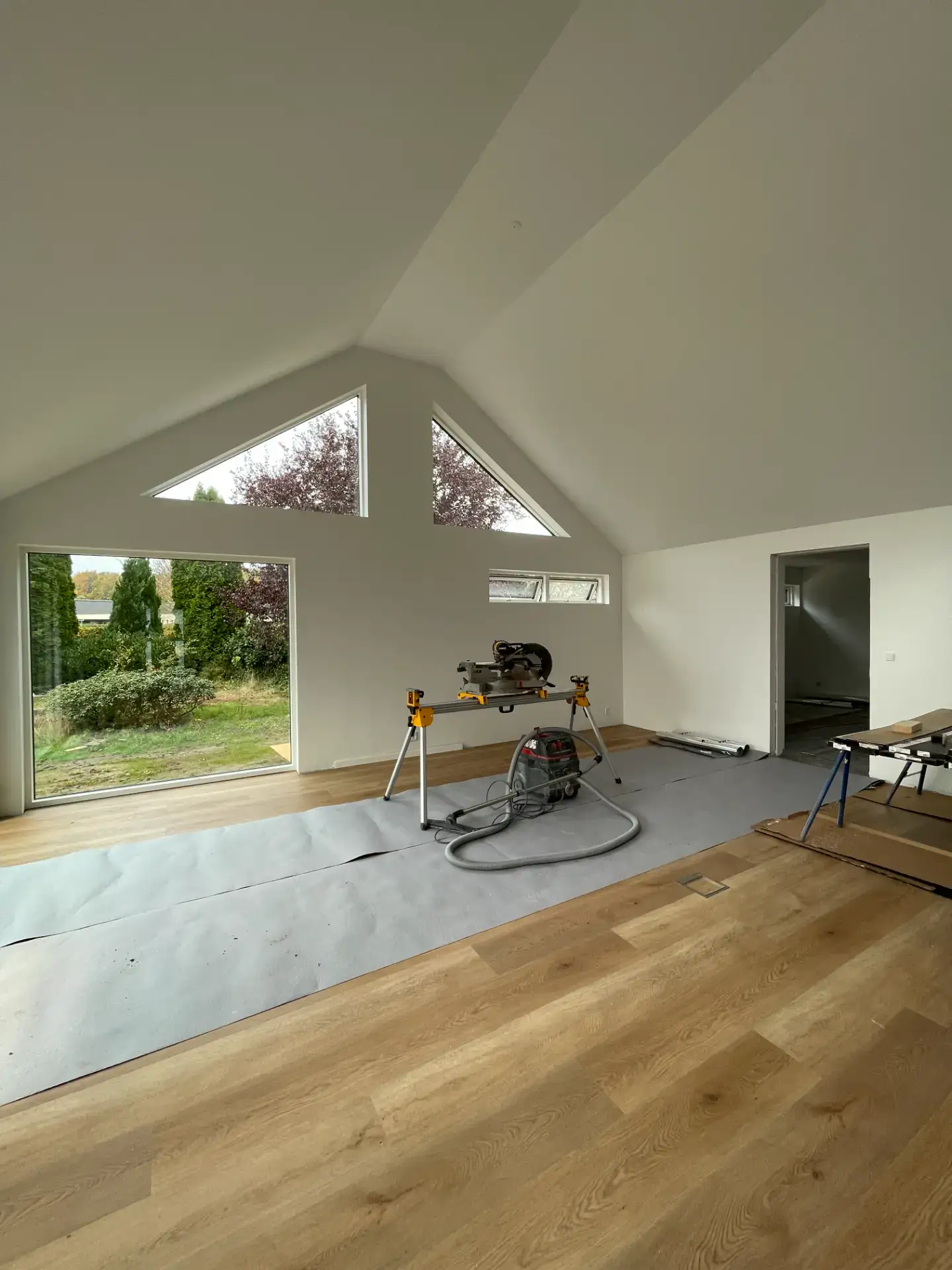 Moderne bolig med store vinduer og trægulv under renovering.