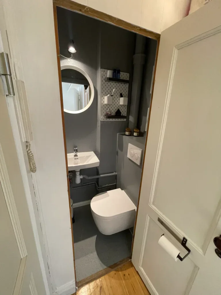 Moderne badeværelse med væghængt toilet, rund spejl og opbevaringshylder.